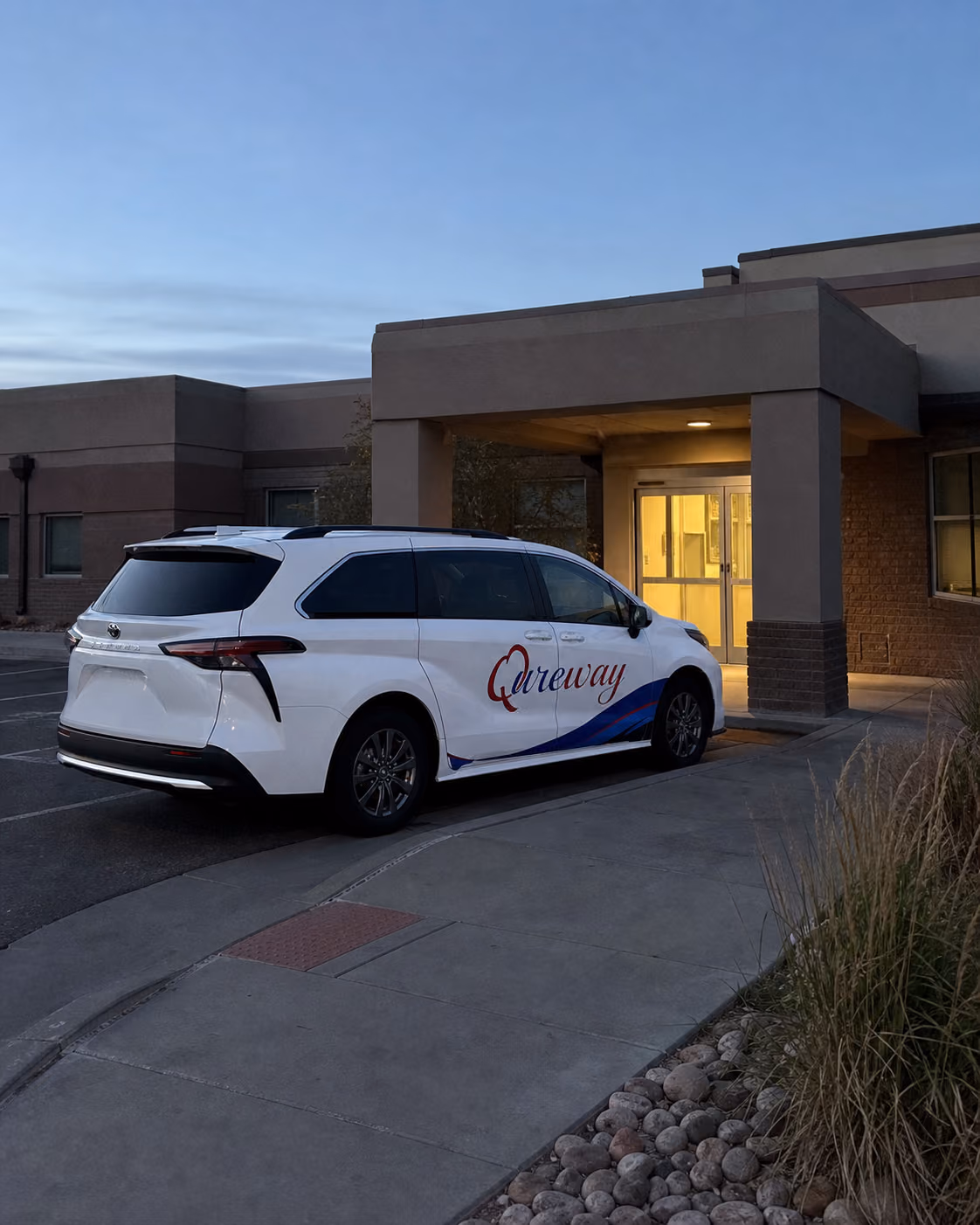 A Qureway wheelchair-accessible van waiting outside a dialysis clinic at dawn
