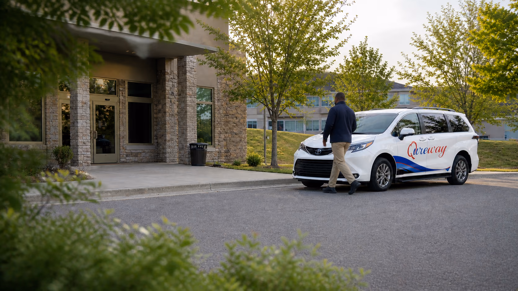 A Qureway driver walking from the wheelchair-accessible van toward a medical clinic entrance